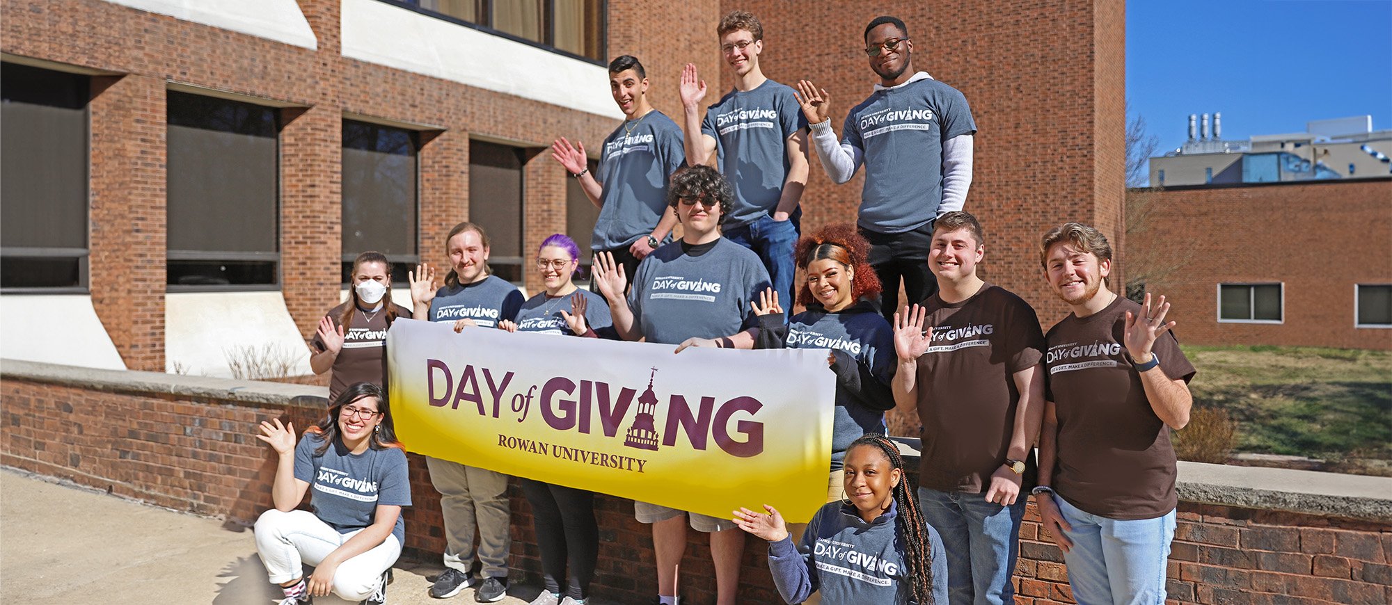 Twelve Rowan University Students stand holding a Day of Giving Banner.