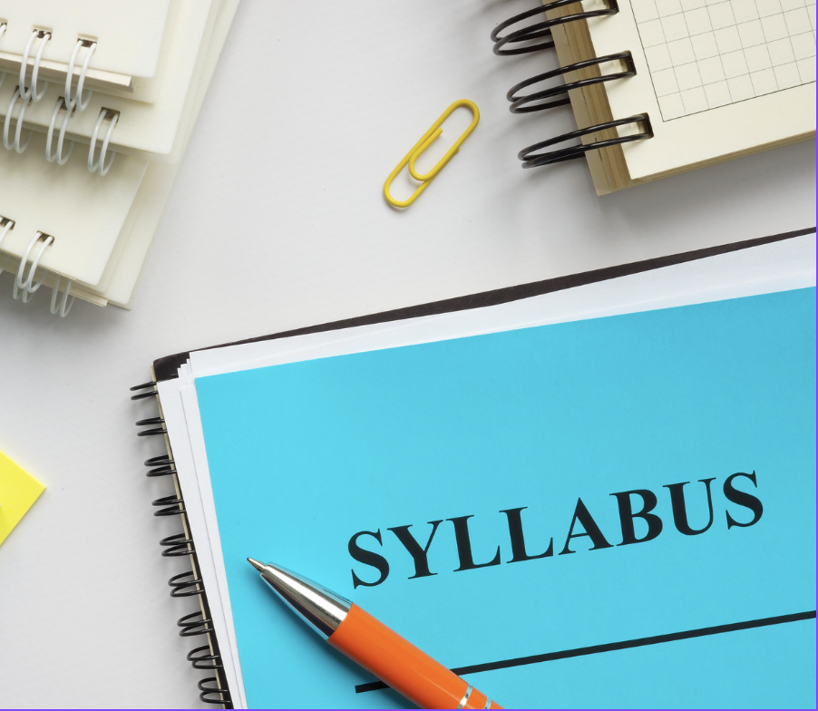 The bottom half of the image features a notebook with a blue sheet of paper and a pen resting on top of it. The blue paper reads, “Syllabus” in black type. 