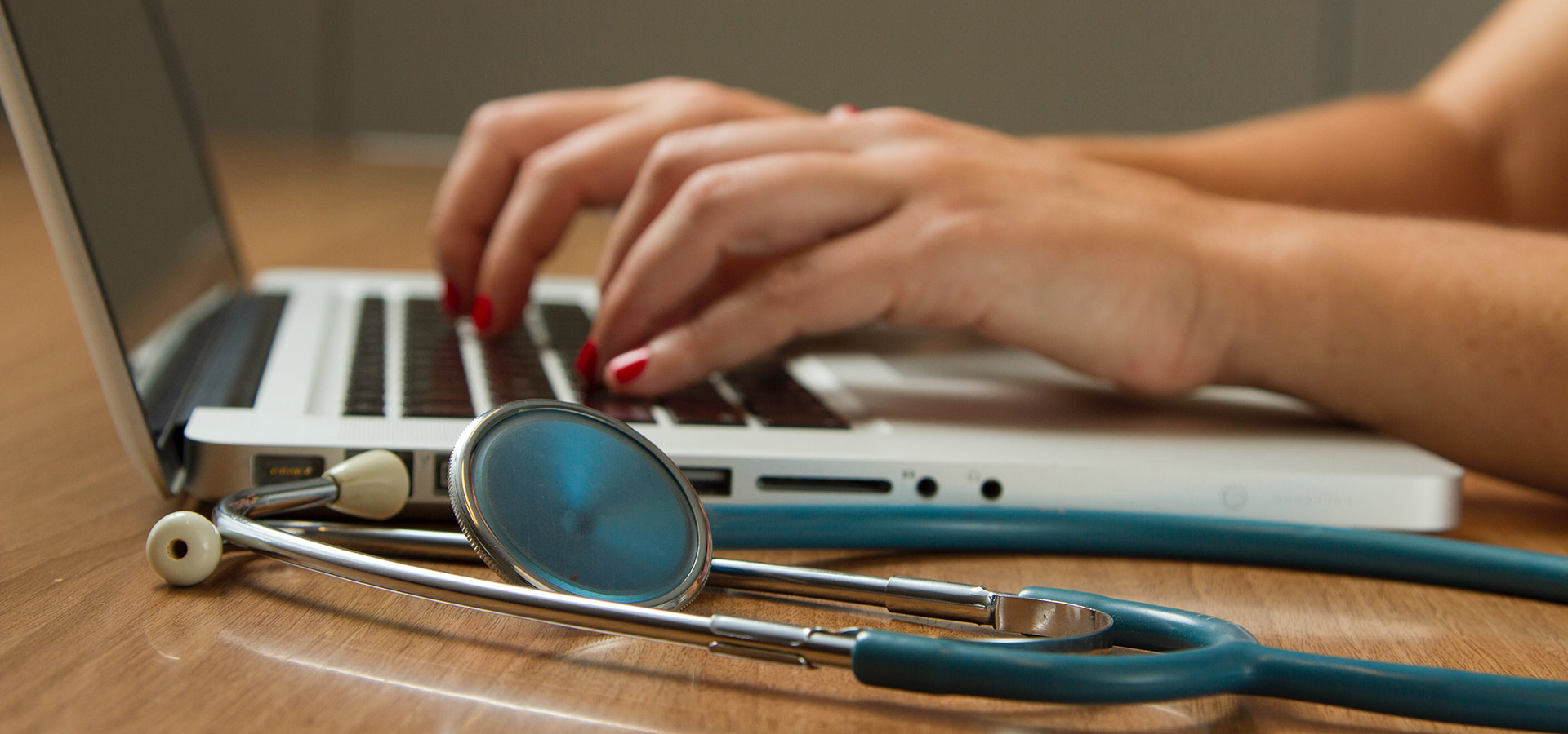 person typing on laptop next with stethoscope on the table