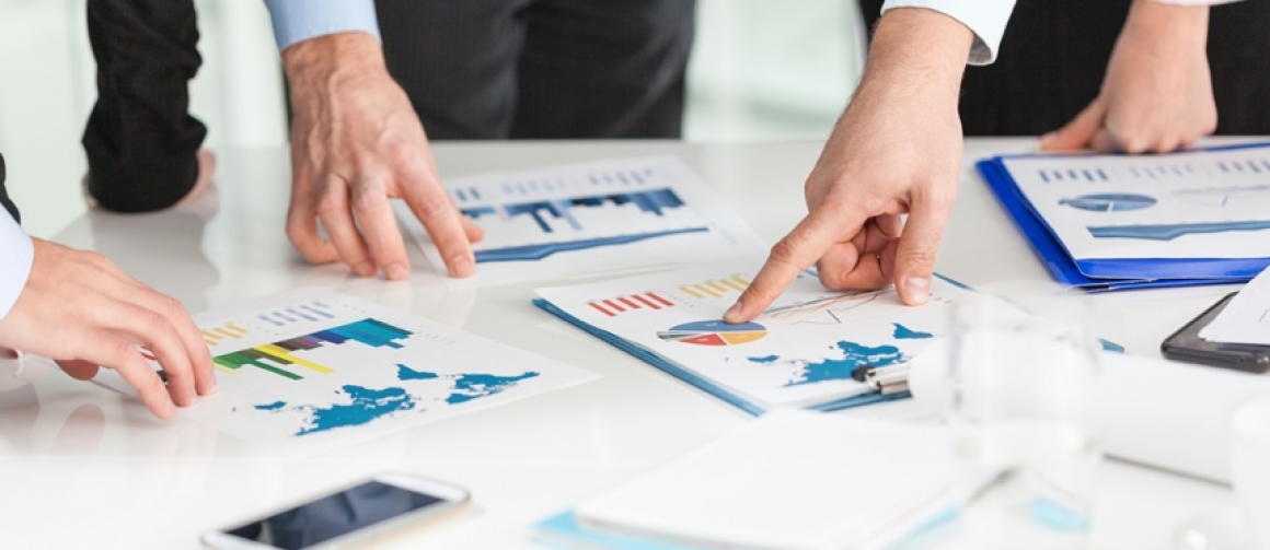 Close up of hands pointing to charts and graphs printed out scattered across a table.