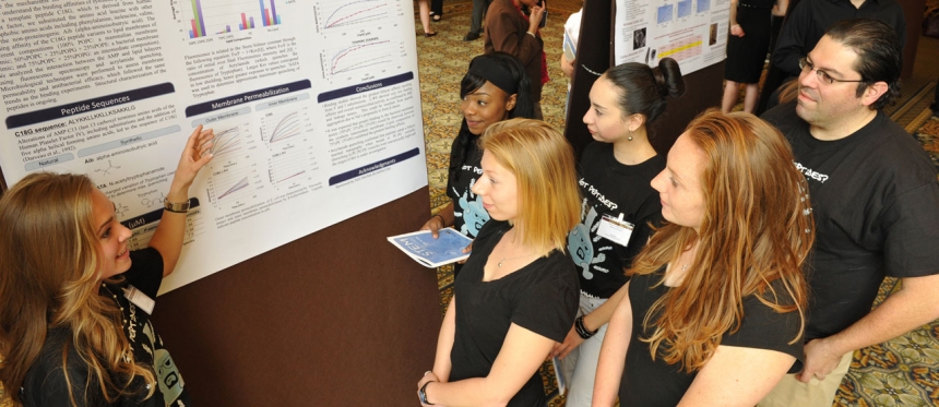 Female student showing a group of students charts on a poster board.