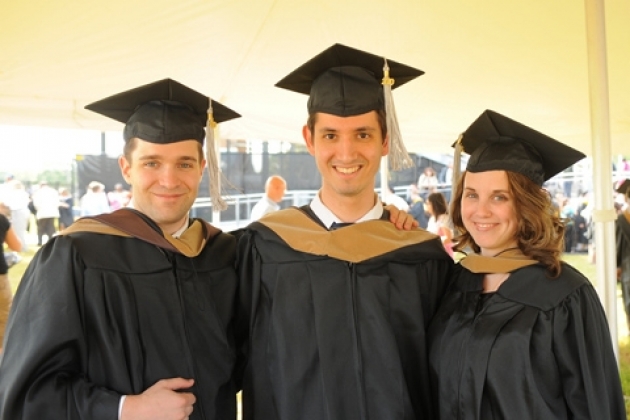 Three students standing together in graduation caps and gowns.