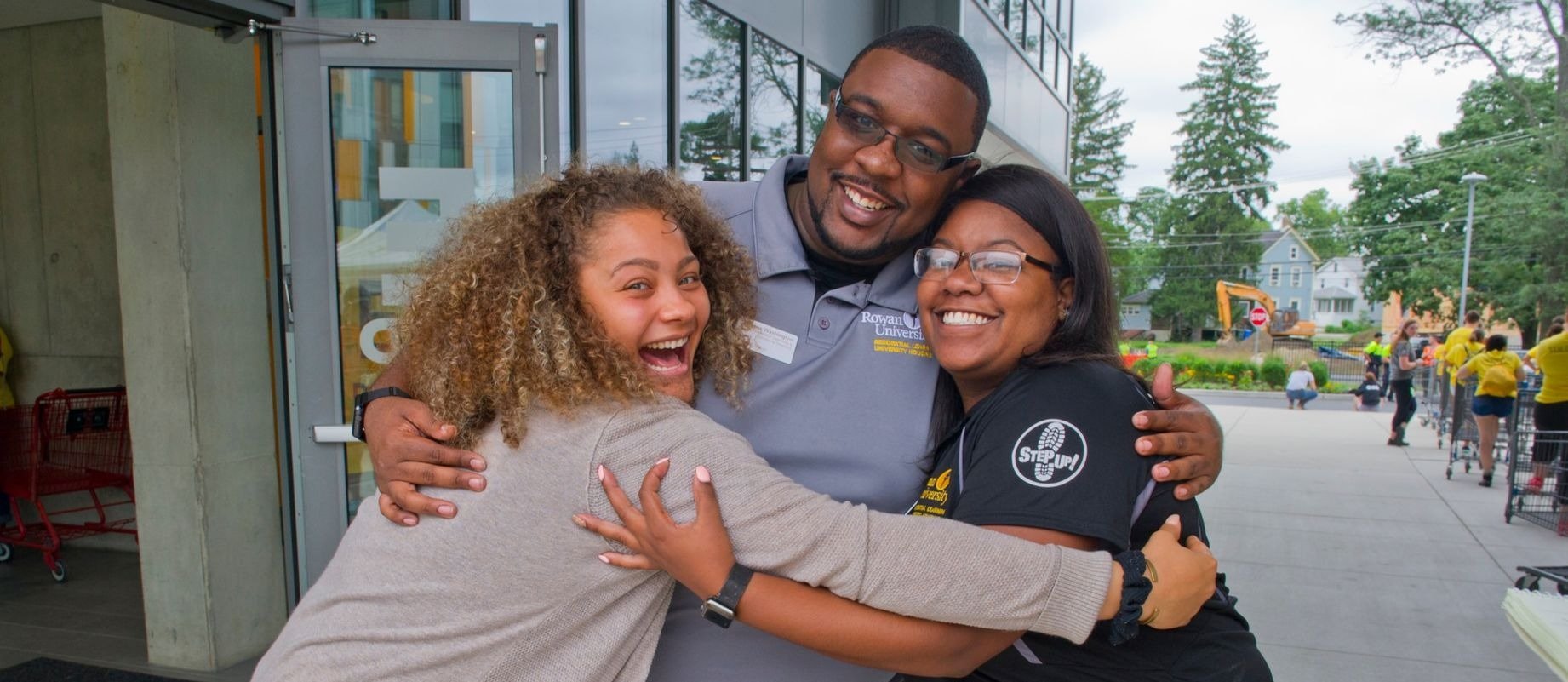 three individuals smiling and hugging on Rowan's campus 