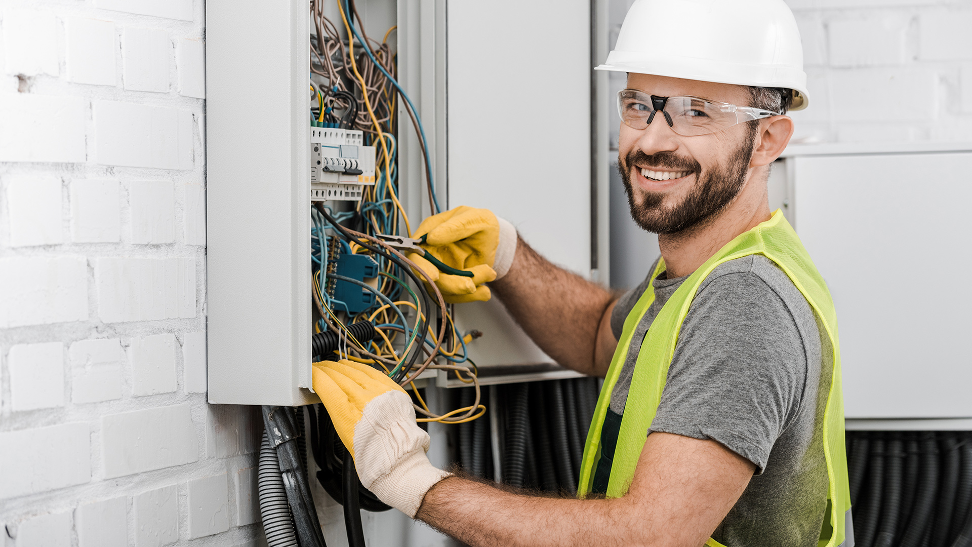 Electrical engineer in hardhat and vest working on electrical panel.