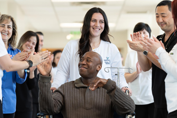 nurse escorting a patient in a wheelchair as medical staff clap and cheer around them.