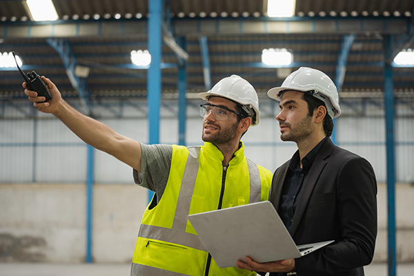 Two engineers wearing hardhats reviewing plans on a laptop.