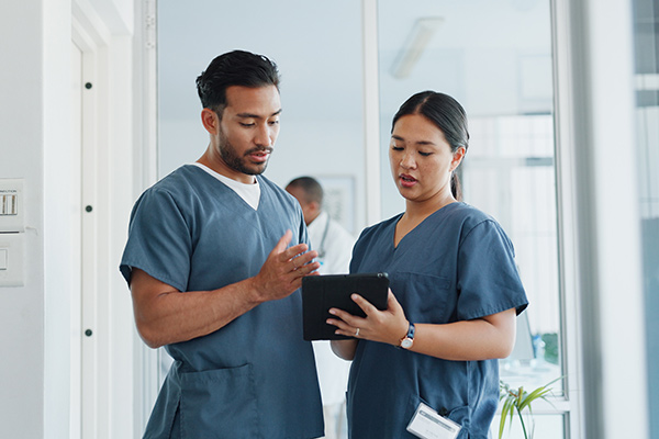 Two nurses holding a clipboard and looking down while having a discussion.
