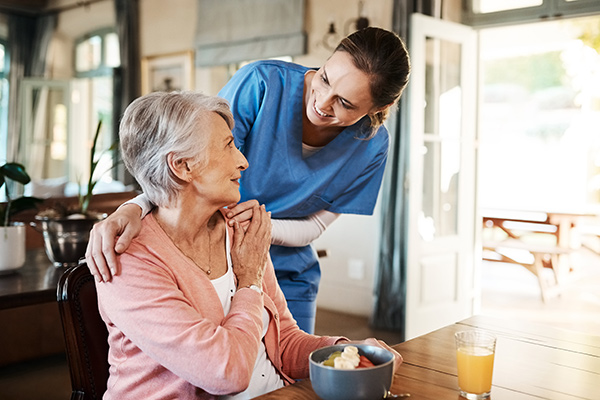 Nurse in scrubs, helping elderly patient eat and drink.