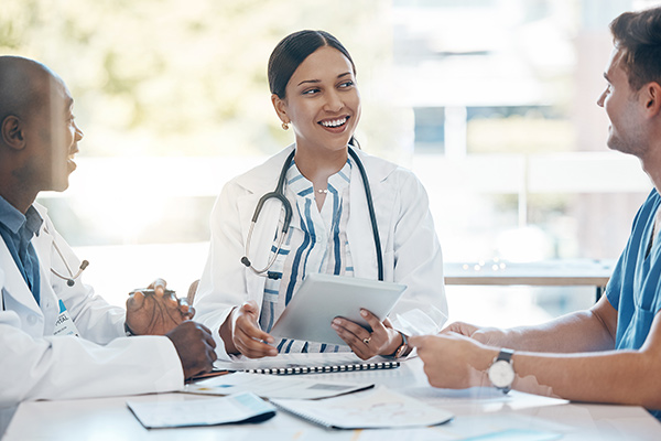 Three nurses having a discussion around a table while reviewing paperwork.