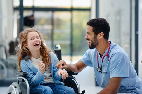 Pediatric nurse, smiling and laughing with a child in a wheelchair.