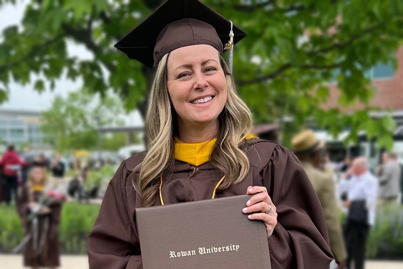 nursing student smiling, wearing cap and gown and holding a Rowan University degree
