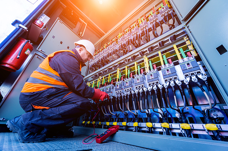 Electrical engineer wearing protective gear, working on large electrical panel.