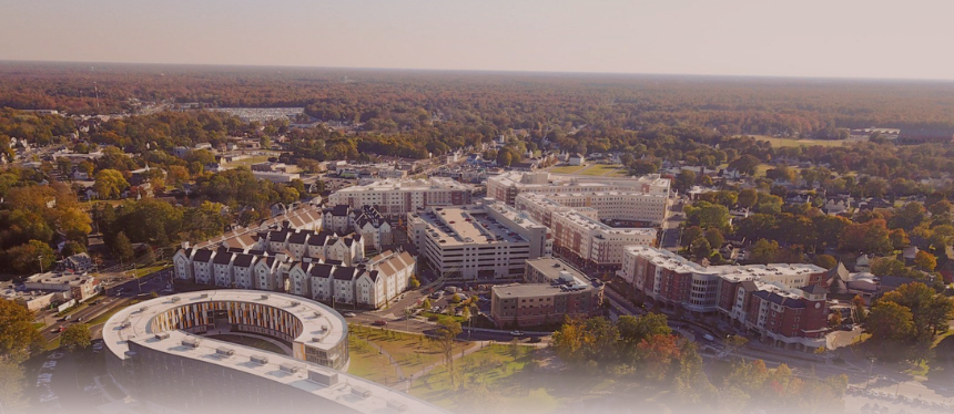 Aerial view of a university campus with modern buildings surrounded by autumn-colored trees, creating a serene and expansive atmosphere under a clear sky.