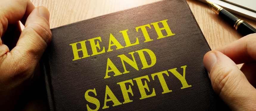 Hands hold a brown binder labeled "Health and Safety" in yellow text on a wooden table. A pen rests nearby, emphasizing a profesHands hold a brown binder labeled "Health and Safety" in yellow text on a wooden table. A pen rests nearby, emphasizing a professional tone.sional tone.
