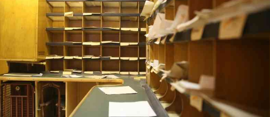 A vintage mail sorting room with wooden cubbyholes filled with letters and papers. The room conveys an organized yet nostalgic atmosphere.