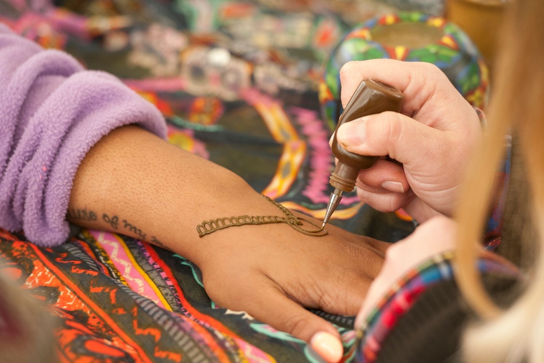 1 girl painting another girls hand with a henna tattoo