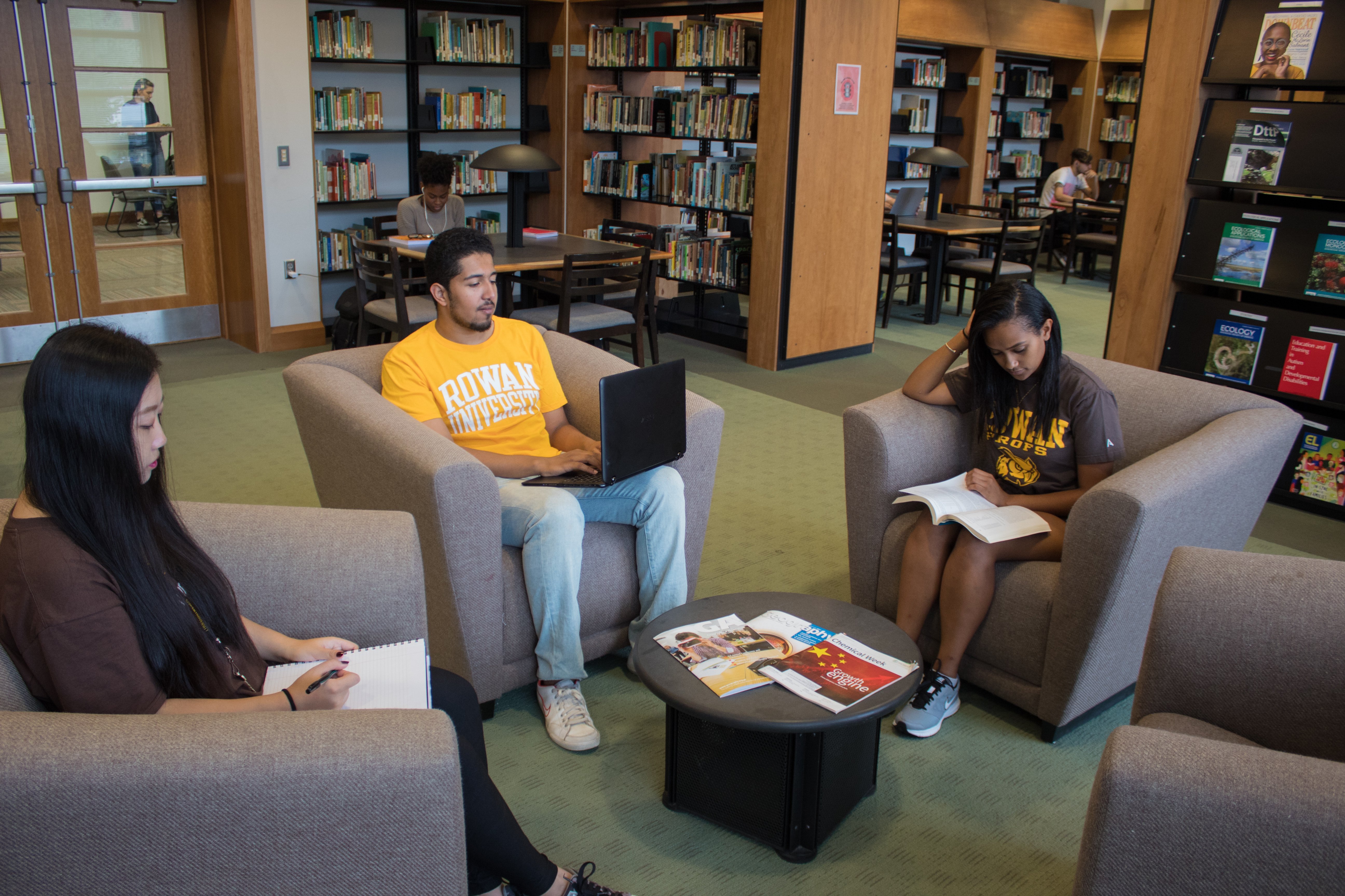 Three students sitting on chairs in the library.