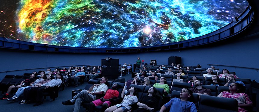An audience views a colorful nebula on the planetarium screen.