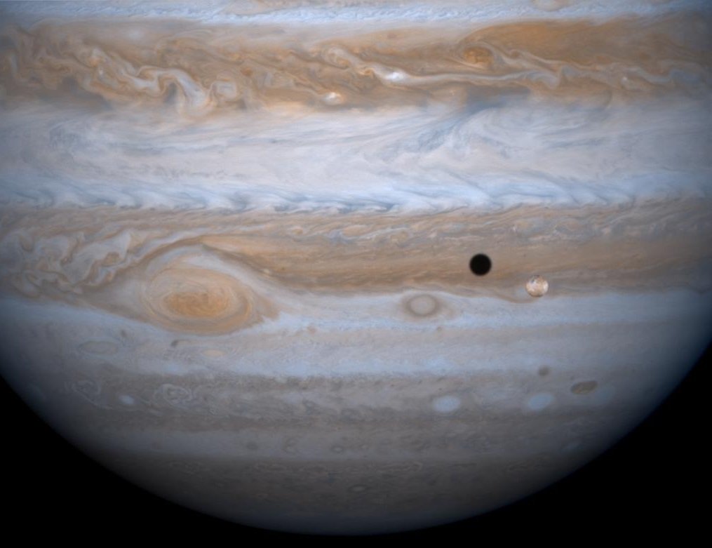 Io transits Jupiter as seen from the Cassini spacecraft. Io, the small yellow-orange circle in the lower right corner and its shadow. The shadow is a black disc up and to the left of the moon.
