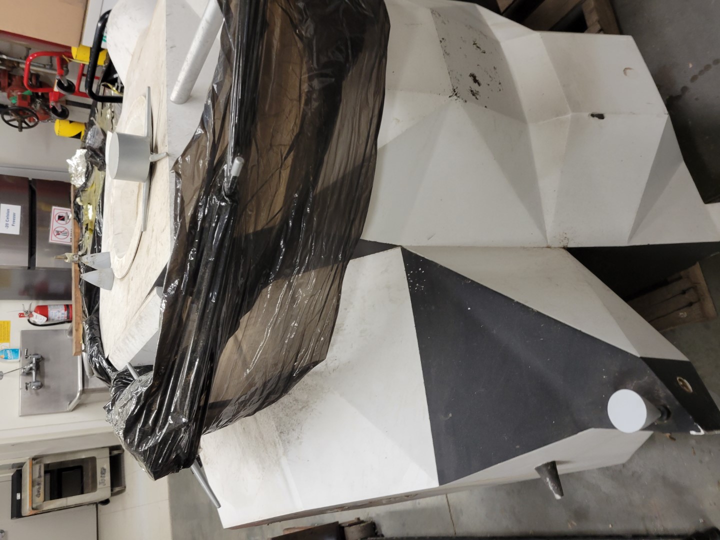 The top section of the lunar lander model wrapped in black plastic and covered in dirt, scratches and scuff marks
