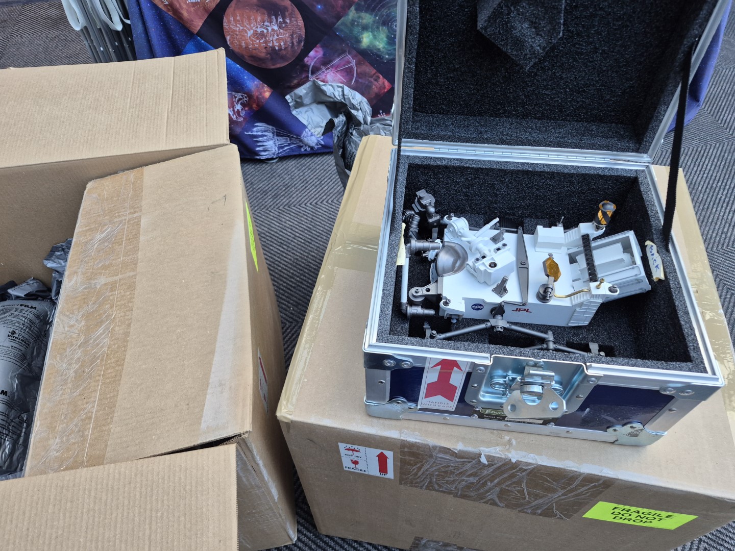 Model of Perseverance sitting in a protective crate and surrounded by shipping boxes.