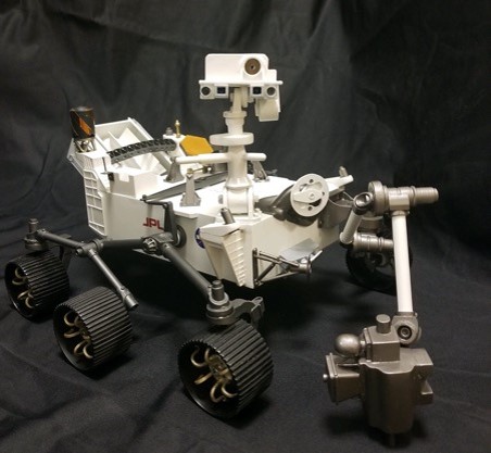 A desktop-sized model of the Perseverance rover surrounded by a gray background