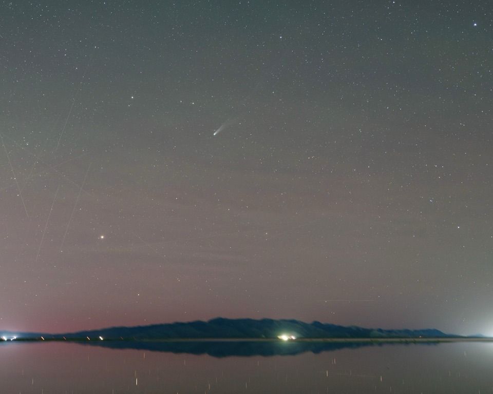 Comet Lemmon is visible in a starry sky reflected in a lake.