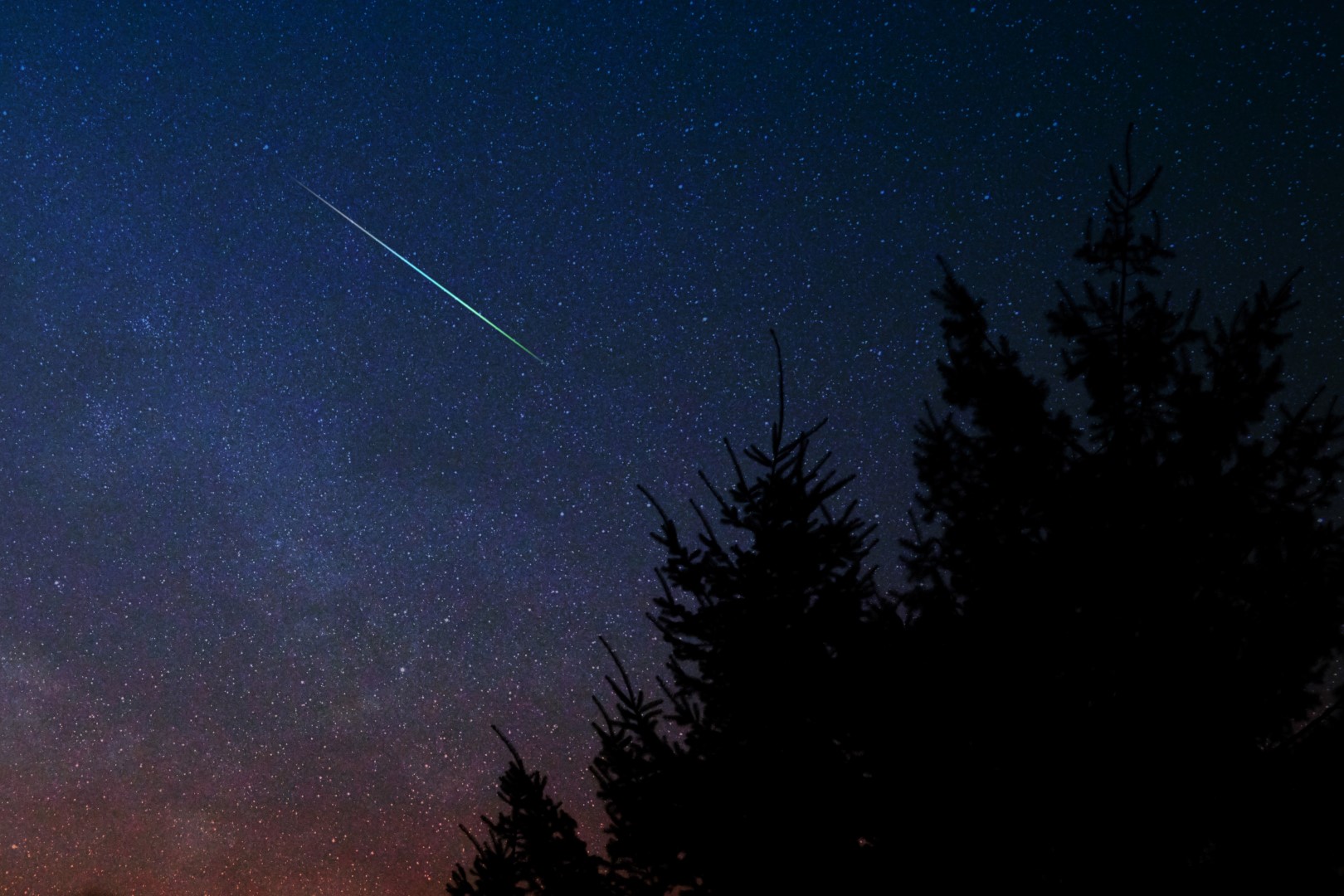 A bright meteor streaks across a starry sky.