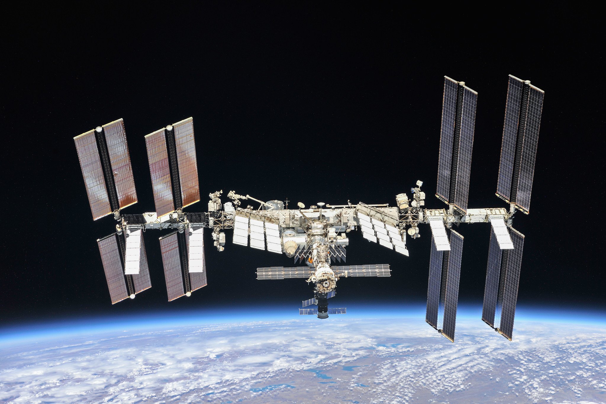 The International Space Station as photographed by astronauts aboard a Soyuz spacecraft. It hangs above the Earth in the image.