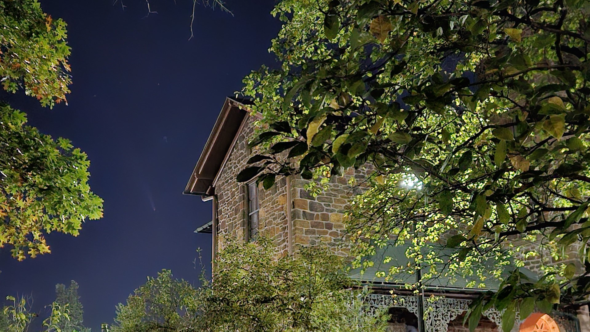 A faint comet is framed between branches and a stone building