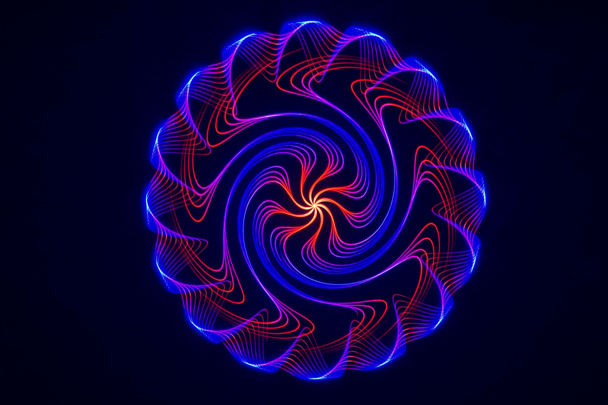 Circular spiral pattern of blue, red, and yellow laser lines against a black background.