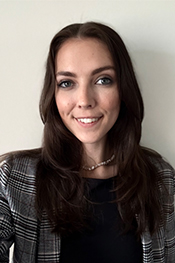 Aleksis Grace smiles at the smaera while wearing a black blouse and a black and white blazer