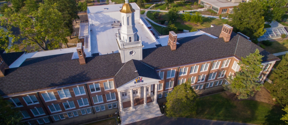 An aerial view of Bunce Hall with golden light from a sunset making the red bricks of the building stand out. 
