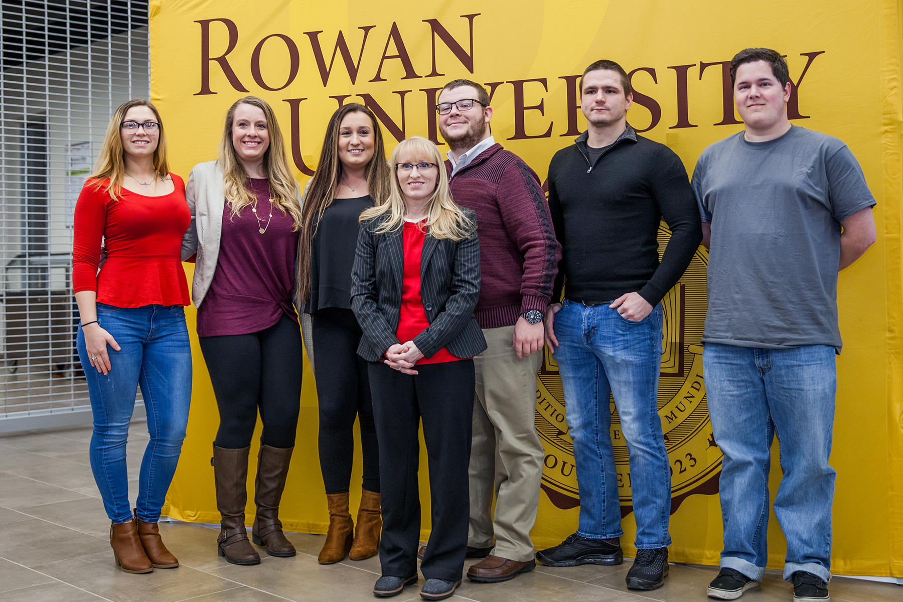A group of seven women and three men standing in front of a Rowan University banner.