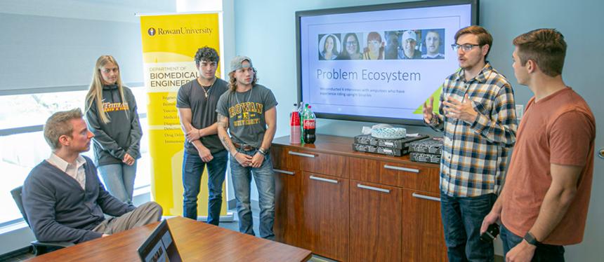 Rowan University students presenting a project during a classroom presentation with a Biomedical Engineering banner in the background.