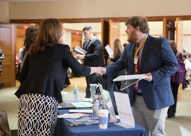 Two individuals shaking hands at a career fair event