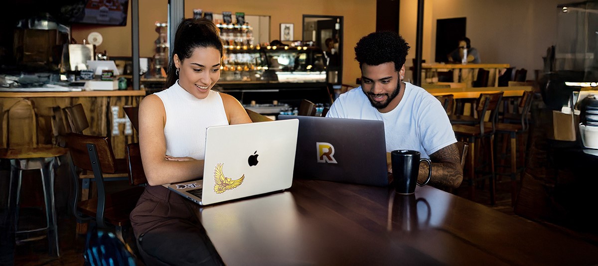 Two students working on laptops together at a coffee shop