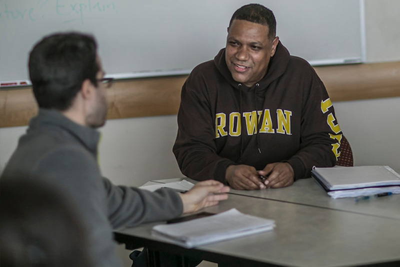Three individuals sit at a table with open notebooks. 
