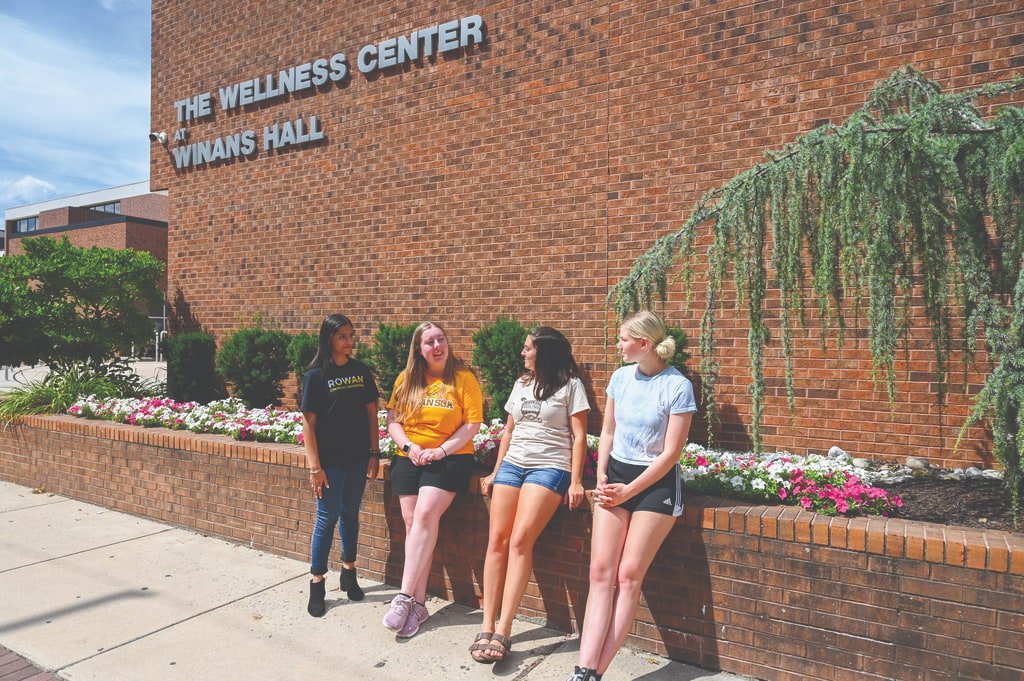 Students leaning against the Wellness Center building.
