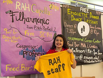A student poses with information for Rowan After Hours (RAH) events.