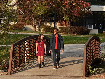 Two students walk over a bridge on campus.