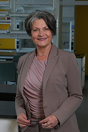TBES dean, Dianne Langford, smiles at the camera while standing in a lab; she is holding her glasses and wearing a mauve and pink pantsuit