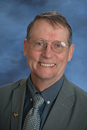 SNHP Dean, Peter Rattigan, smiles at the camera while wearing glasses and a grey suit