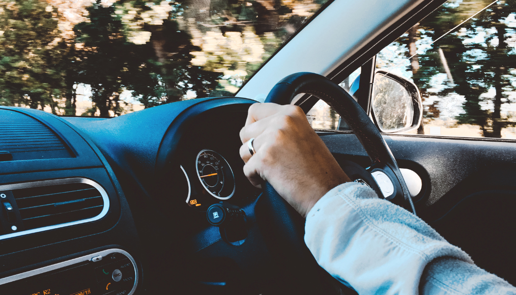 a shot of a steering wheel and a hand from someone driving it in a car