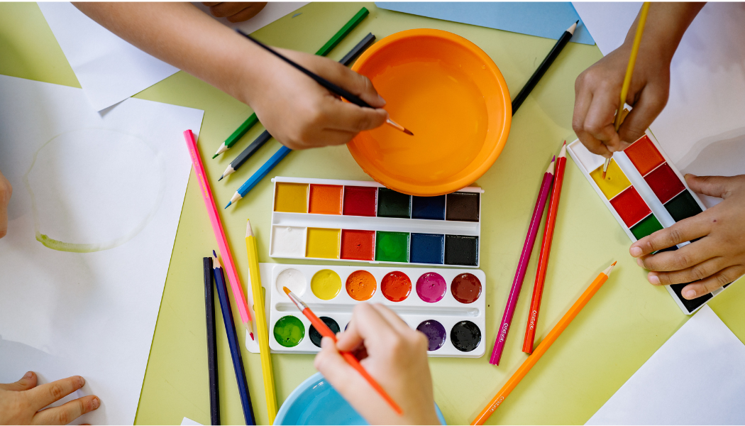 hands that are painting on paper and drawing with colored pencils